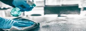 Zwei Hände putzen einen Metalltisch als Maßahme für die Hygiene